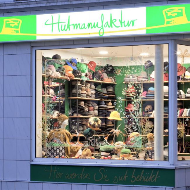Hutmacherin_web Beleuchtetes Ladengeschäft der Hutmanufaktur von außen